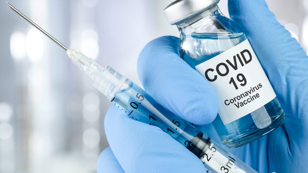Healthcare cure concept with a hand in blue medical gloves holding Coronavirus, Covid 19 virus, vaccine vial